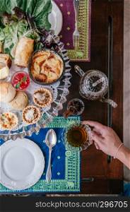 Traditional elegance English afternoon tea with scone, assorted tart and puff pastries on old wood table, hand holding tea cup top view