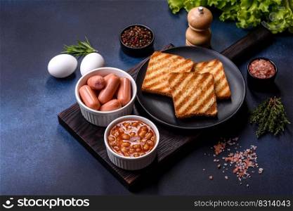 Traditional English breakfast with eggs, toast, sausages, beans, spices and herbs on a grey ceramic plate against a dark concrete background. Traditional English breakfast with eggs, toast, sausages, beans, spices and herbs on a grey ceramic plate