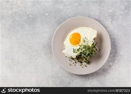 Traditional English breakfast with fried eggs with arugula microgreen in gray ceramic plate on gray concrete old background. Top view.
