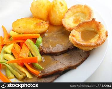 Traditional English meal of roast beef and yorkshire puddings (popovers), with julienned courgette (zucchini) and carrots, oven roasted potatoes and gravy.