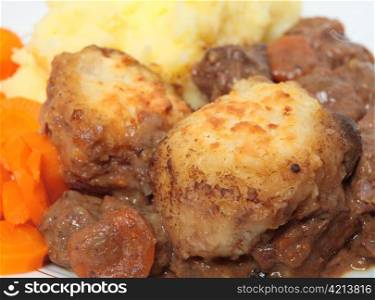 Traditional English suet dumplings on a steak and kidney stew, served with mashed potato and carrots