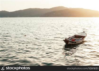 Traditional fishing boat docked in the sea at sunset. Old wooden row boat in the sea, mount island in the background in the sun rays at sunset. Travel, vacation, getaway, loneliness, solitude concept