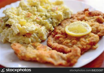 Traditional fried pork schnitzel with Czech potato mayonnaise salad and lemon slice on top.