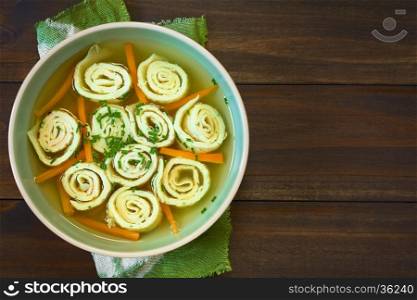 Traditional German Flaedlesuppe and Austrian Frittatensuppe based on consomme with rolls or stripes of pancake or crepe garnished with chives, photographed overhead on wood with natural light (Selective Focus, Focus on the soup)