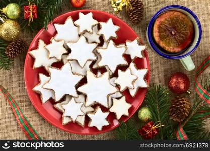 Traditional German Zimtsterne (cinnamon stars) Christmas cookies made of ground almonds, cinnamon, egg white and confectioner&rsquo;s sugar, meringue on top, photographed overhead with Christmas decoration and mulled wine on the side. German Zimtsterne Christmas Cookies