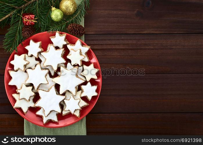 Traditional German Zimtsterne (cinnamon stars) Christmas cookies made of ground almonds, cinnamon, egg white and confectioner&rsquo;s sugar, meringue on top, photographed overhead with Christmas decoration on the side. German Zimtsterne Christmas Cookies