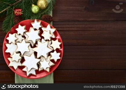 Traditional German Zimtsterne (cinnamon stars) Christmas cookies made of ground almonds, cinnamon, egg white and confectioner&rsquo;s sugar, meringue on top, photographed overhead with Christmas decoration on the side. German Zimtsterne Christmas Cookies