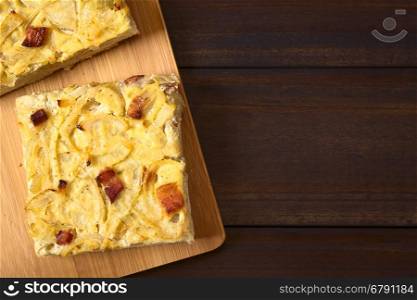 Traditional German Zwiebelkuchen savory onion cake pieces made of onion, bacon and cream sauce on yeast dough, photographed overhead on dark wood with natural light (Selective Focus, Focus on the top of the cake pieces)