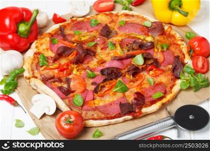 Traditional home made pizza with ham and salami on white kitchen wooden table