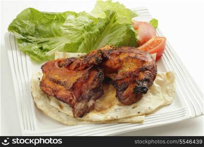 Traditional indian tandoori chicken pieces, served on flat bread with a salad and tomatoes, side view, a delicacy from the Punjab region of north India and Pakistan.
