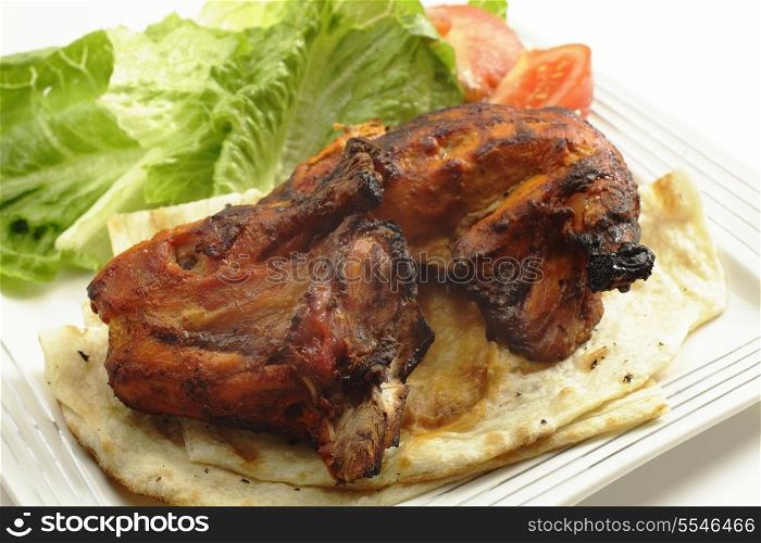 Traditional indian tandoori chicken pieces, served on flat bread with a salad and tomatoes, side view, a delicacy from the Punjab region of north India and Pakistan