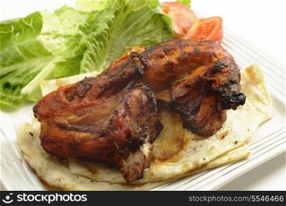 Traditional indian tandoori chicken pieces, served on flat bread with a salad and tomatoes, side view, a delicacy from the Punjab region of north India and Pakistan