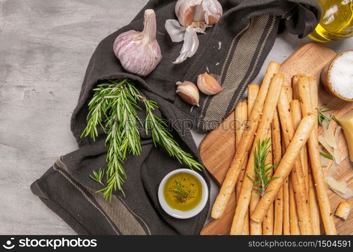 Traditional italian breadsticks grissini with rosemary, parmesan cheese, olive oil, garlic and salt on a gray background. top view. Flat lay with copy space