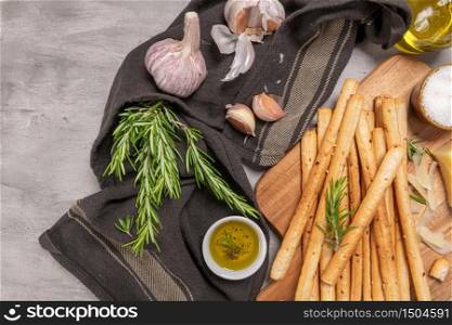 Traditional italian breadsticks grissini with rosemary, parmesan cheese, olive oil, garlic and salt on a gray background. top view. Flat lay with copy space