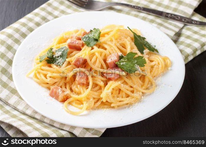 Traditional Italian cuisine, pasta Carbonara with ham and parmesan cheese served on white plate on black slate background.. Pasta Carbonara served on a white plate.