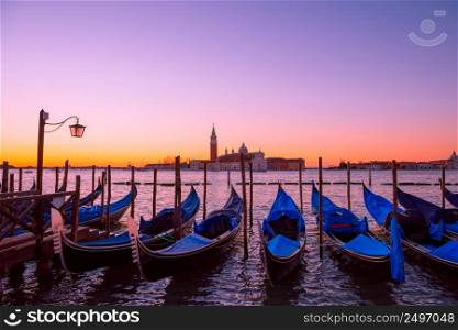 Traditional Italian gondolas moored to the poles in Europe Venice near the city center and Saint Mark square with a background view of the church of San Giorgio Maggiore at sunrise