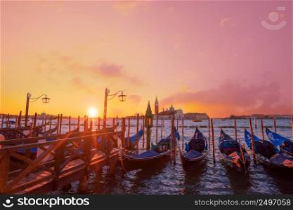 Traditional Italian gondolas moored to the poles in Europe Venice near the city center and Saint Mark square with a background view of the church of San Giorgio Maggiore at sunrise time