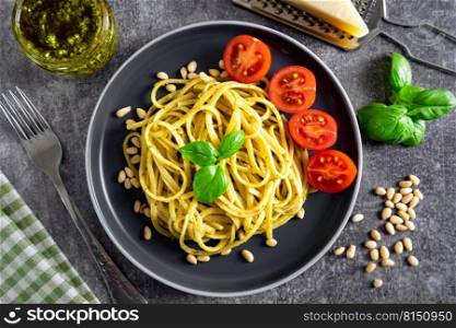 Traditional italian pasta with fresh vegetables, parmesan cheese, basil leaves, pine nuts and pesto sauce in black bowl on grey stone background. Top view, flat lay. Traditional italian pasta pesto