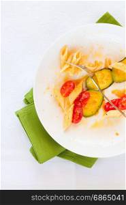 Traditional italian penne pasta with zucchini and cherry tomatoes already eaten seen from above. Italian penne pasta with zucchini and cherry tomatoes