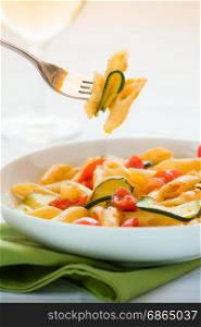 Traditional italian penne pasta with zucchini and cherry tomatoes seasoned with oil and pepper ready to eat. Italian penne pasta with zucchini and cherry tomatoes