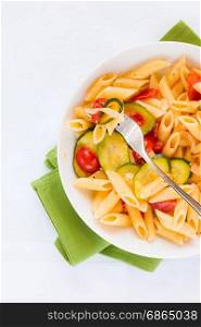 Traditional italian penne pasta with zucchini and cherry tomatoes seasoned with oil and black pepper seen from above. Italian penne pasta with zucchini and cherry tomatoes