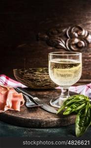 Traditional Italian snack: dry cured ham, melon and glass of wine with cutlery at dark wooden background, front view