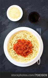 Traditional Italian Spaghetti alla Marinara (spaghetti with tomato sauce) in bowl with red wine and grated cheese, photographed overhead on slate with natural light (Selective Focus, Focus on the dish)