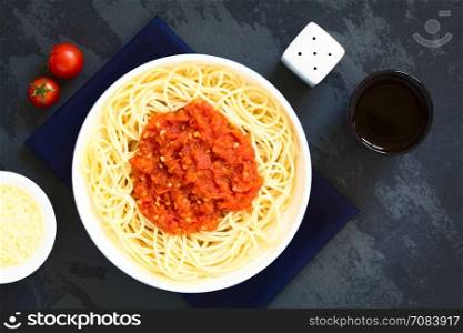 Traditional Italian Spaghetti alla Marinara (spaghetti with tomato sauce) in bowl with red wine and grated cheese on the side, photographed overhead on slate with natural light