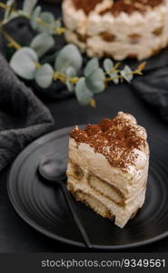 Traditional italian tiramisu cake on black plate