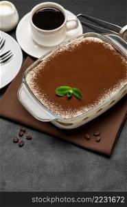 Traditional Italian Tiramisu dessert in glass baking dish and cup of fresh hot espresso coffee on concrete background or table. Traditional Italian Tiramisu dessert in glass baking dish and cup of fresh hot espresso coffee on concrete background