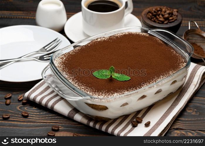 Traditional Italian Tiramisu dessert in glass baking dish and cup of fresh hot espresso coffee on wooden background or table. Traditional Italian Tiramisu dessert in glass baking dish and cup of fresh hot espresso coffee on wooden background