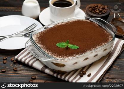 Traditional Italian Tiramisu dessert in glass baking dish and cup of fresh hot espresso coffee on wooden background or table. Traditional Italian Tiramisu dessert in glass baking dish and cup of fresh hot espresso coffee on wooden background
