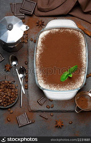 Traditional Italian Tiramisu dessert in glass baking dish and pieces of chocolate bar on concrete background or table. Traditional Italian Tiramisu dessert in glass baking dish, mocha coffee maker and pieces of chocolate bar on concrete background