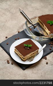 Traditional Italian Tiramisu dessert in glass baking dish and portion on grey concrete background.. Traditional Italian Tiramisu dessert in glass baking dish and portion on grey concrete background