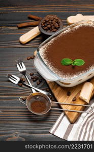 Traditional Italian Tiramisu dessert in glass baking dish and savoiardi cookies on cutting serving board on wooden background or table. Traditional Italian Tiramisu dessert in glass baking dish and savoiardi cookies on cutting serving board on wooden background