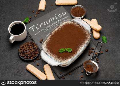Traditional Italian Tiramisu dessert in glass baking dish, cup of coffee and savoiardi cookies on stone serving board with chalk inscription sign on concrete background or table. Traditional Italian Tiramisu dessert in glass baking dish, cup of coffee and savoiardi cookies on stone serving board with chalk inscription sign on concrete background