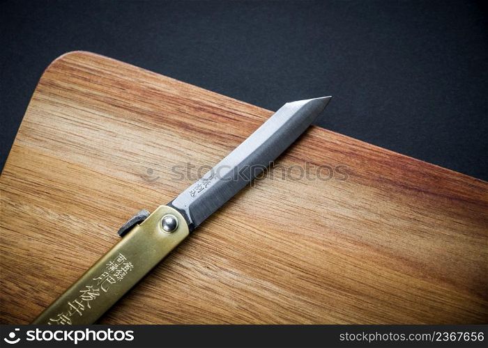 Traditional japanese higonokami pocket knife on a wooden cutting board. Black background. Traditional japanese pocket knife on a wooden cutting board