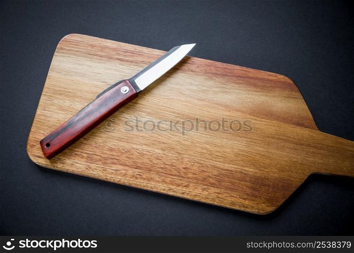Traditional japanese higonokami pocket knife on a wooden cutting board. Black background. Traditional japanese pocket knife on a wooden cutting board
