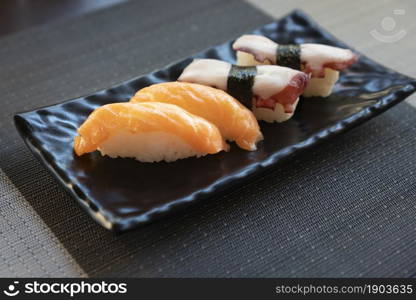 Traditional japanese nigiri sushi with salmon and sushi with octopus on black plate.