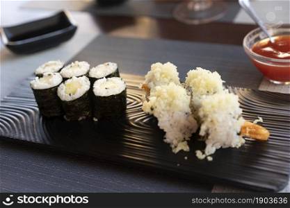 Traditional japanese rolls sushi with cucumbers and rolls sushi with shrimps fried on black plate at restaurant.