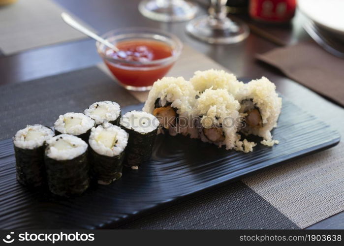 Traditional japanese rolls sushi with cucumbers and rolls sushi with shrimps fried on black plate at restaurant.Background sweet chili sauce.