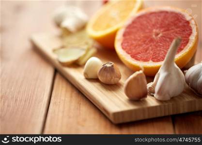 traditional medicine, cooking and ethnoscience concept - garlic, ginger, orange and grapefruit on wooden board