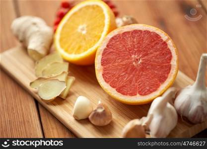 traditional medicine, cooking and ethnoscience concept - ginger, orange, grapefruit and garlic on wooden board