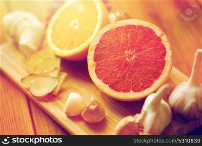 traditional medicine, cooking and ethnoscience concept - ginger, orange, grapefruit and garlic on wooden board. grapefruit, ginger, garlic and orange on board