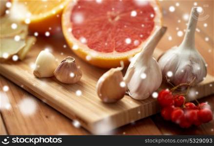 traditional medicine, cooking and ethnoscience concept - orange, grapefruit with ginger and garlic on wooden board over snow. citrus, ginger, garlic and rowanberry on wood