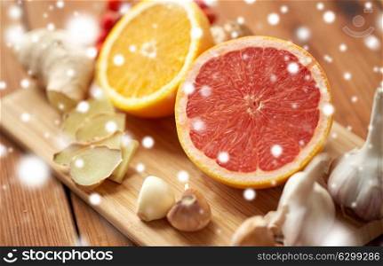 traditional medicine, cooking and ethnoscience concept - orange, grapefruit with ginger and garlic on wooden board over snow. citrus, ginger, garlic and rowanberry on wood