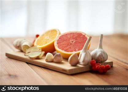 traditional medicine, cooking and ethnoscience concept - orange, grapefruit with ginger and garlic on wooden board