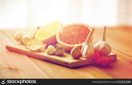 traditional medicine, cooking and ethnoscience concept - orange, grapefruit with ginger and garlic on wooden board. citrus, ginger, garlic and rowanberry on wood