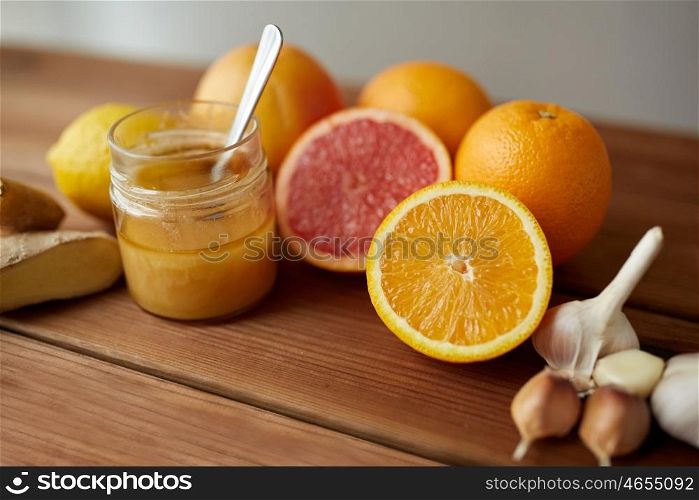traditional medicine, cooking, food and ethnoscience concept - honey, citrus fruits with ginger and garlic on wooden table