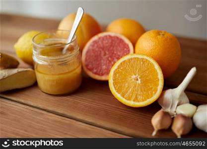 traditional medicine, cooking, food and ethnoscience concept - honey, citrus fruits with ginger and garlic on wooden table